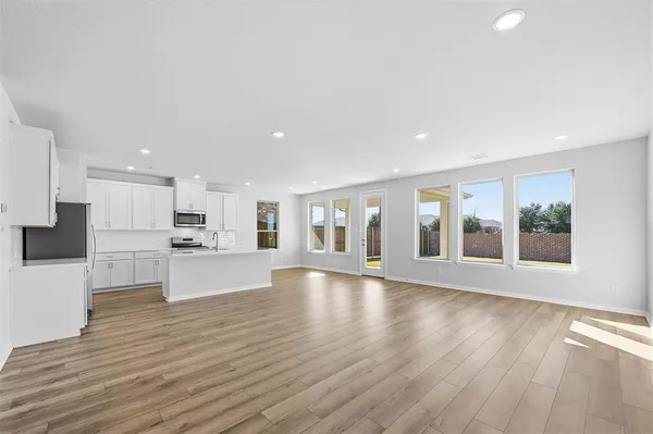 a view of an empty room with kitchen and window