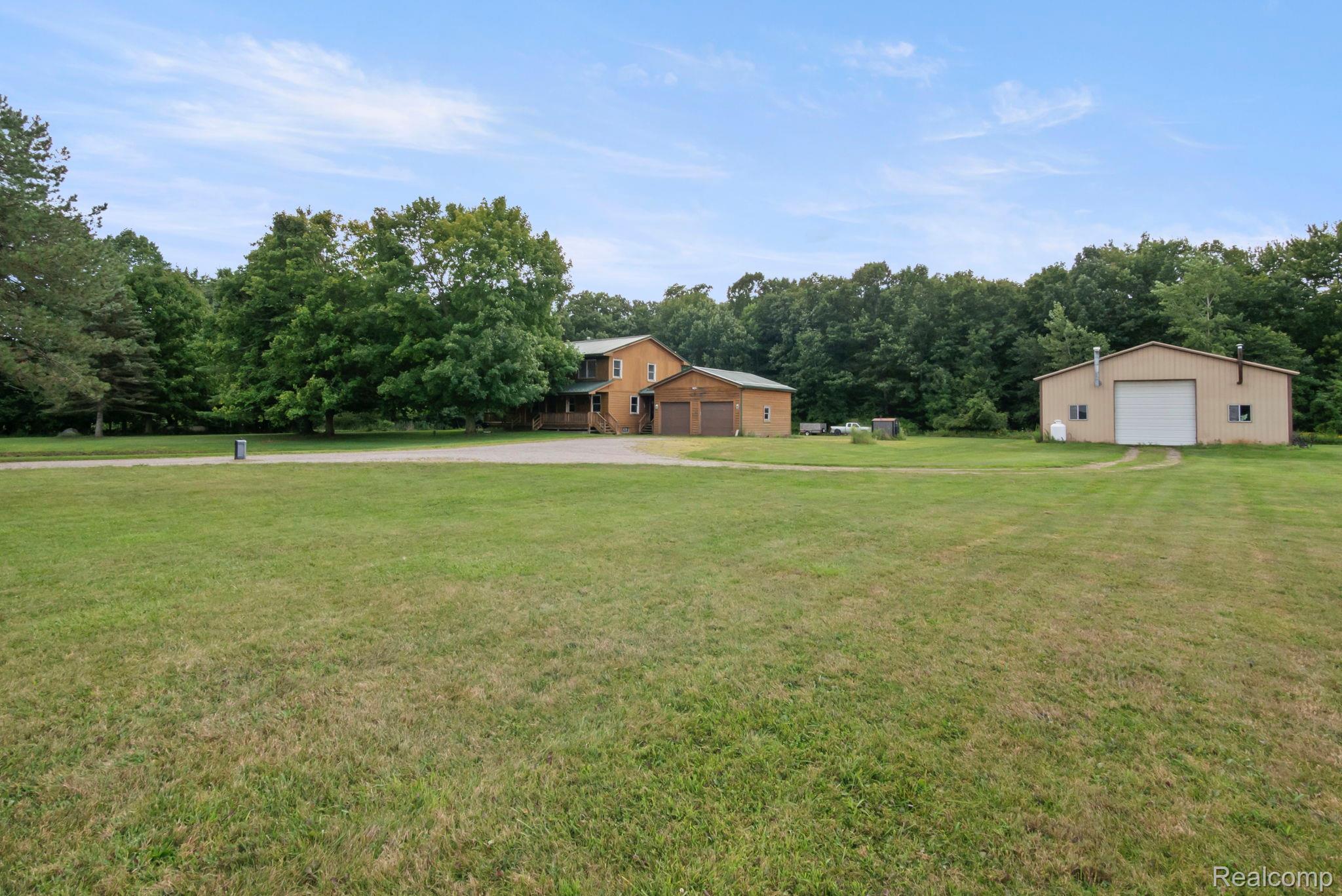 76565 McFadden Road Armada, MI 48005 - Photo 83 of 95 Expansive green lot with established trees, featuring a two-story residence with an attached two-car garage, and a separate large outbuilding with a roll-up door