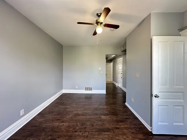 a view of an empty room with wooden floor and a ceiling fan