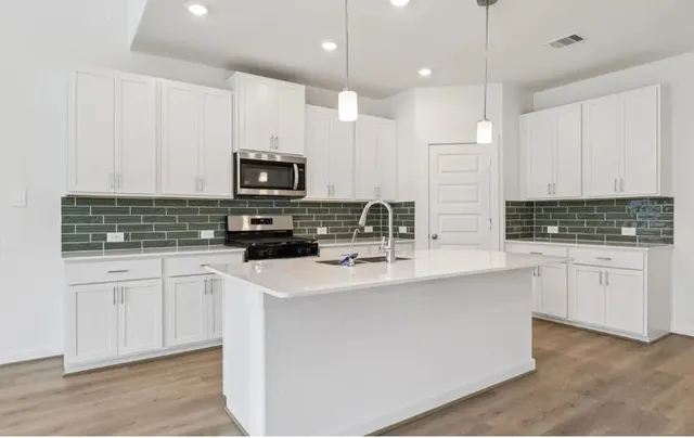 a kitchen with stainless steel appliances granite countertop a stove top oven a sink a refrigerator and white cabinets