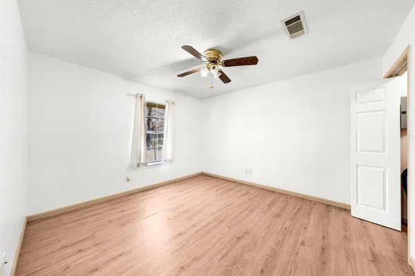 an empty room with wooden floor ceiling fan and windows