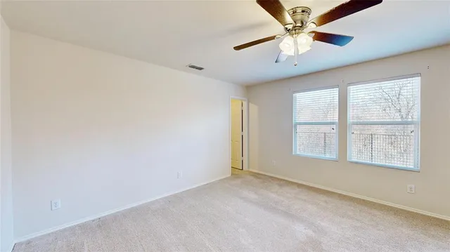an empty room with chandelier fan and windows