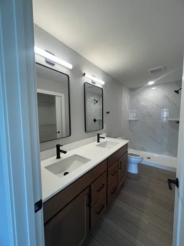 a bathroom with a double vanity sink and mirror with toilet