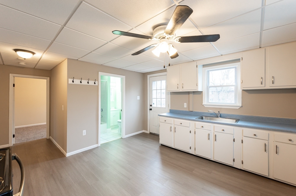 29 Mill Street, Unit B Dracut, MA 01826 - Photo 5 of 37 a kitchen with granite countertop a stove a sink and white cabinets with wooden floor