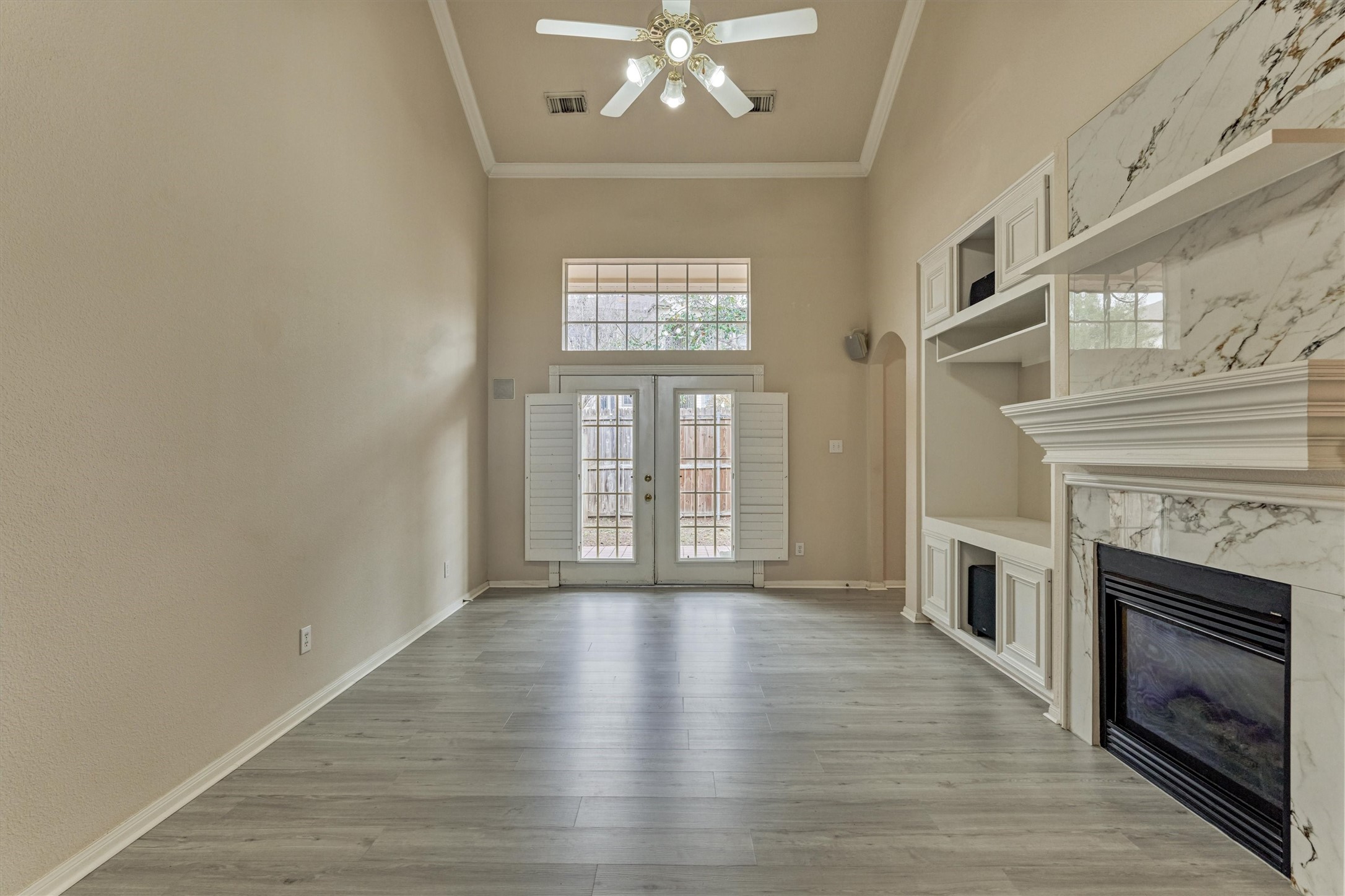 14420 Walters Road, Unit 26 Houston, TX 77014 - Photo 9 of 45 This spacious living room features high ceilings, a ceiling fan, and abundant natural light from large windows and glass doors. It includes a stylish marble fireplace and built-in shelves, complemented by elegant light wood-look flooring.