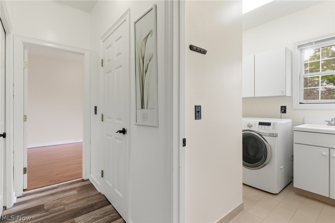 11678 Dunham Road Northfield, OH 44067 - Photo 15 of 38 Dedicated laundry area featuring a front-loading washer, white cabinetry, a utility sink with a window, and tile flooring