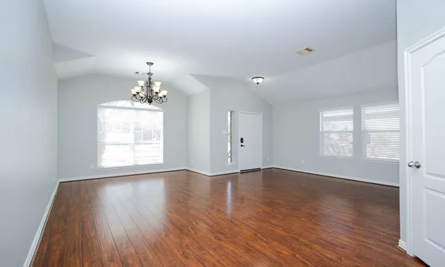 an empty room with wooden floor chandelier and windows