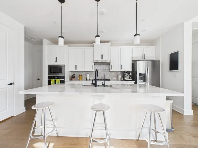 a kitchen with stainless steel appliances granite countertop a refrigerator a stove a kitchen island a sink and white cabinets with wooden floor