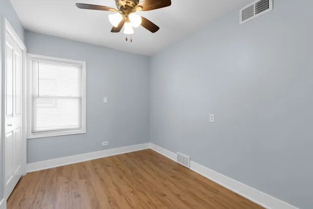 an empty room with wooden floor chandelier fan and windows