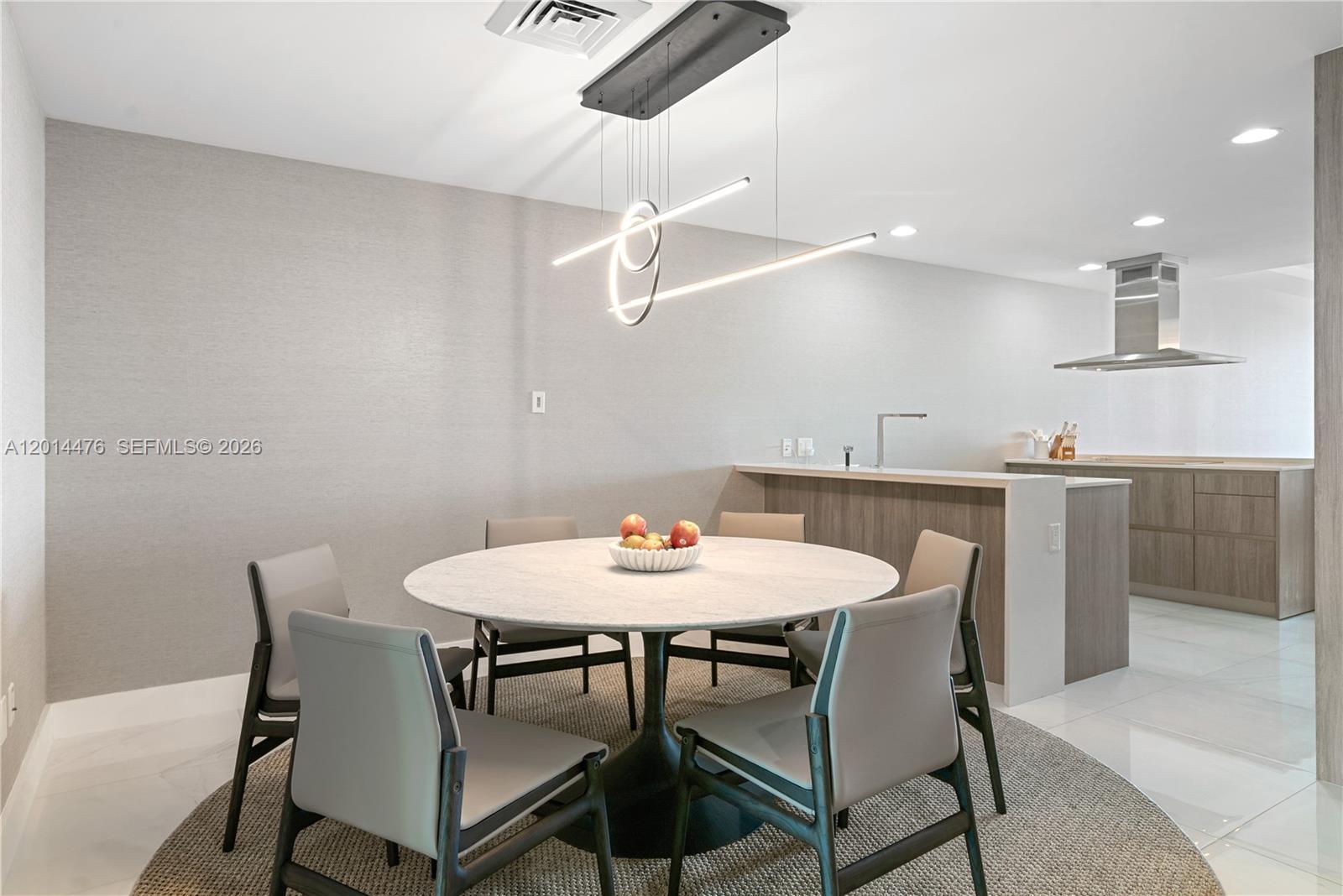 360 Ocean Drive, Unit 1106S Key Biscayne, FL 33149 - Photo 12 of 67 Dining Area – The dining area features a round table, neutral seating, and a sculptural linear chandelier that adds a modern focal point. Its placement beside the kitchen creates an easy flow for everyday dining or hosting.