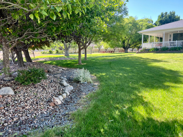 812 East Bates Cyn Road Tooele, UT 84074 - Photo 98 of 144 Spacious green lawn surrounded by mature trees, featuring a stone and gravel landscape bed, and a covered porch