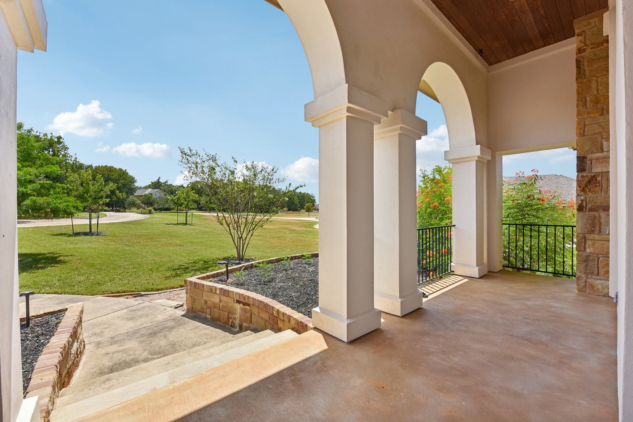163 Powder Horn Road Bastrop, TX 78602 - Photo 4 of 34 Arched columns frame a covered stone patio overlooking a sprawling, manicured green lawn.