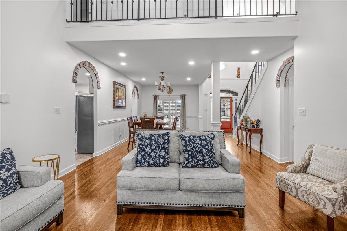 744 Southern Home Road Collierville, TN 38017 - Photo 4 of 24 Spacious living area featuring hardwood flooring, recessed lighting, white wall paneling, brick archways, and an upper-level balcony with iron railings