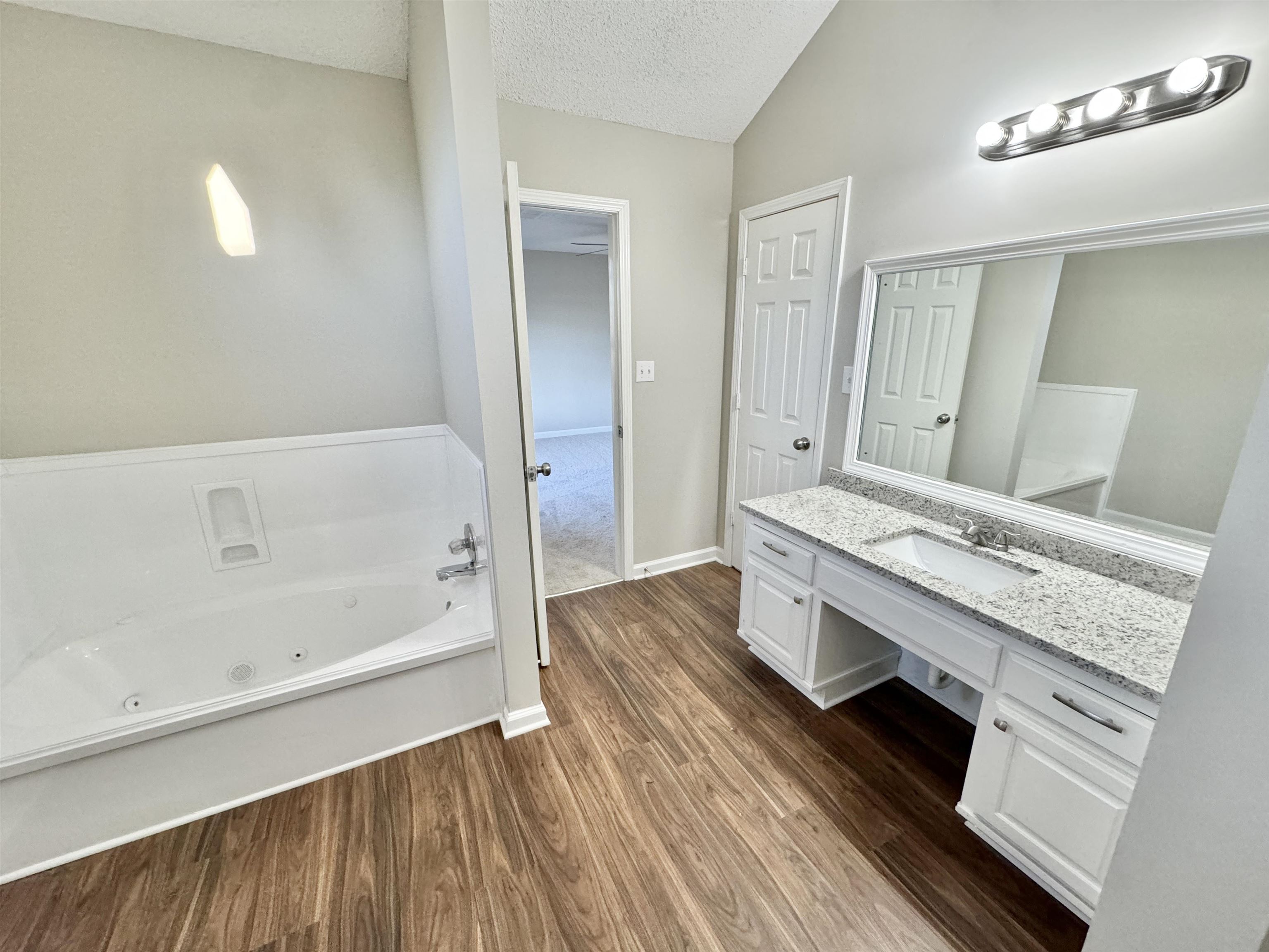775 Portersville Road Atoka, TN 38004 - Photo 16 of 37 Bathroom with vaulted ceiling, hardwood / wood-style floors, a tub to relax in, vanity, and a textured ceiling