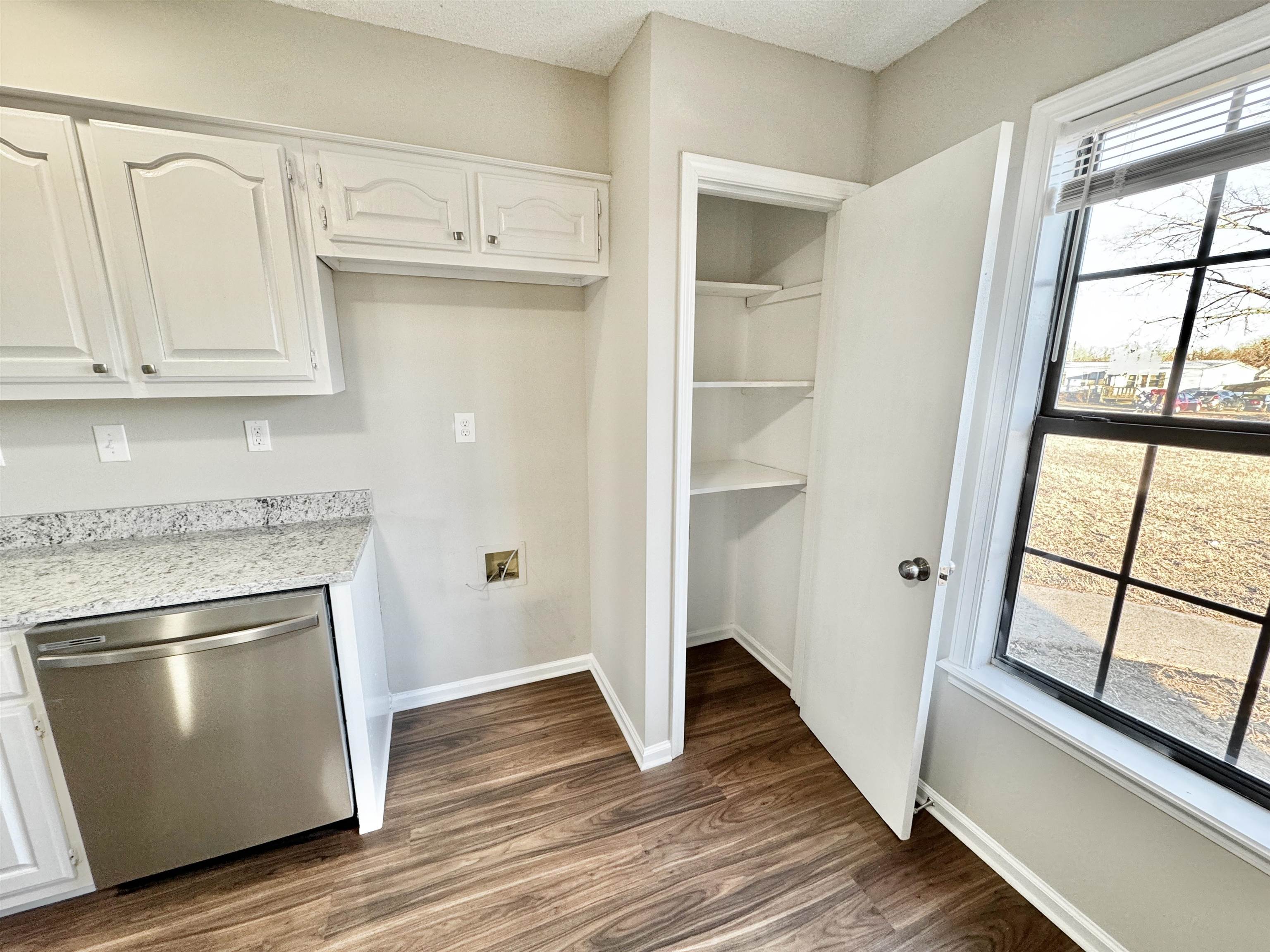 Kitchen with stainless steel dishwasher, dark hardwood / wood-style floors, and white cabinets