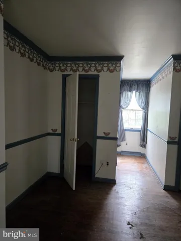 a view of a refrigerator in kitchen and an empty room with wooden floor