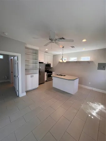 a room with chandelier fan and kitchen view