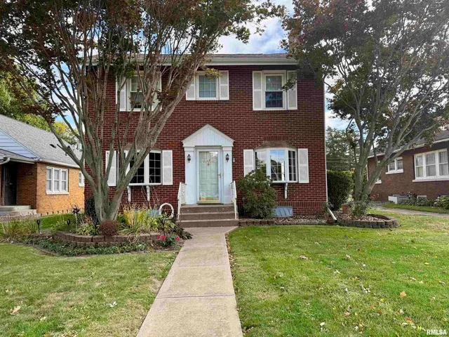 a front view of a house with garden and trees