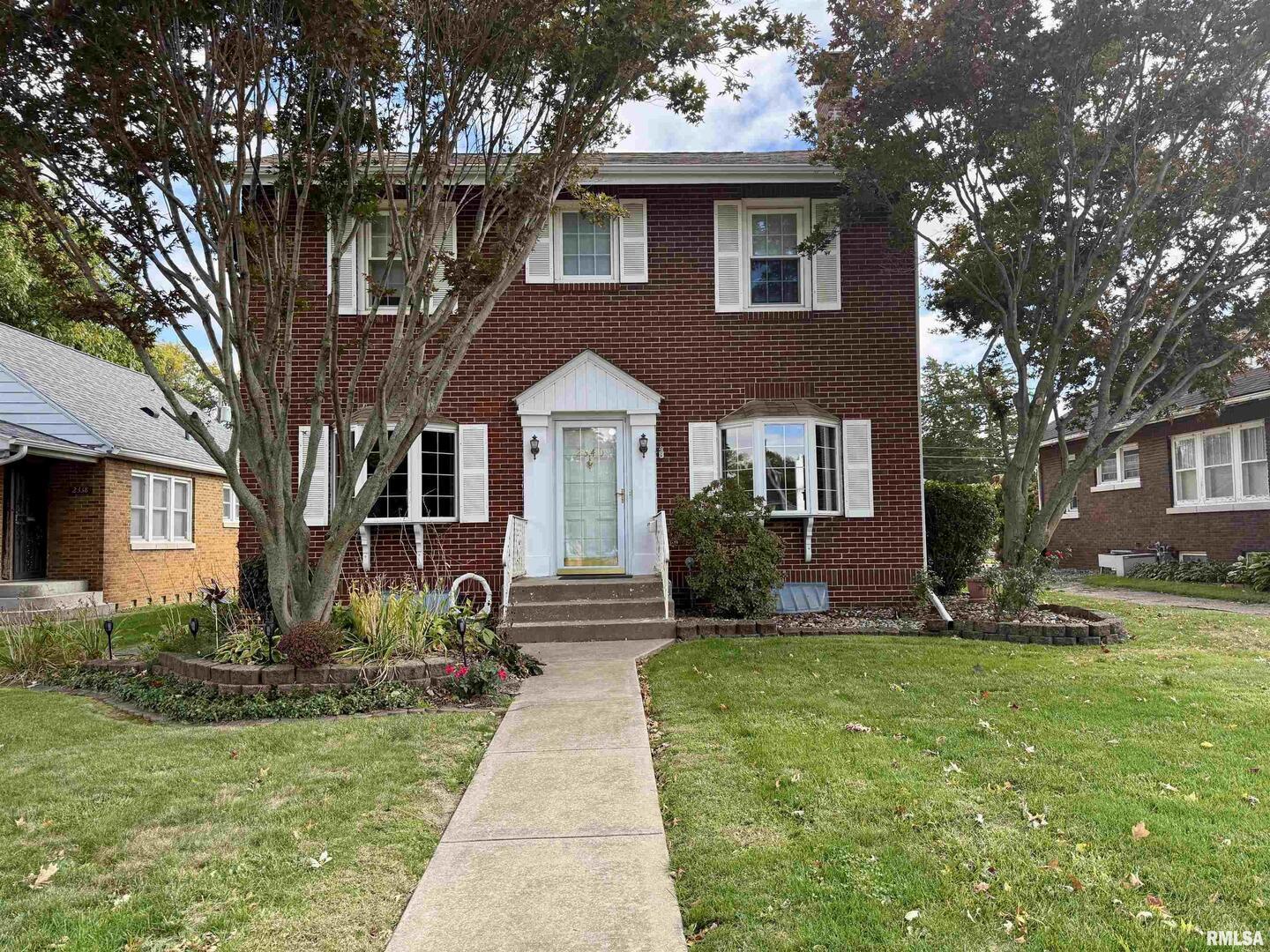 a front view of a house with garden and trees