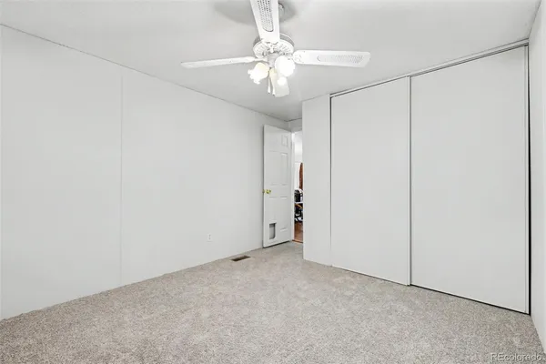 an empty room with chandelier fan and closet area