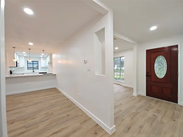 a view of an empty room and kitchen with wooden floor