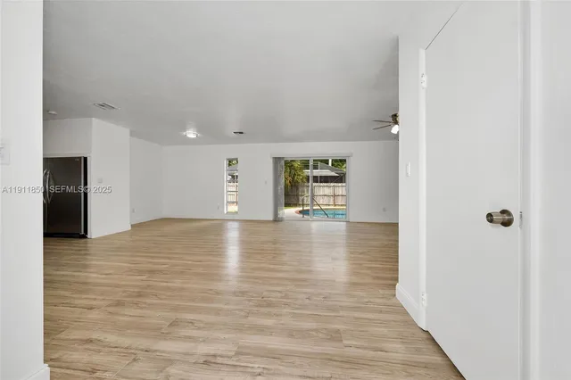 a view of an empty room with wooden floor and a kitchen