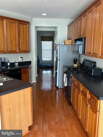 a kitchen with stainless steel appliances a stove a sink a refrigerator white cabinets and wooden floor