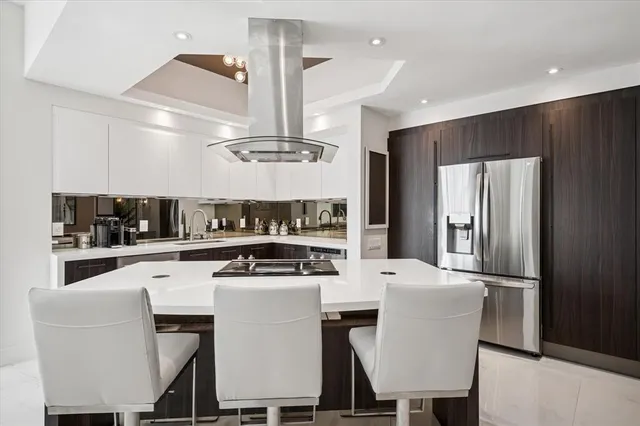 a kitchen with stainless steel appliances kitchen island granite countertop a dining table chairs and a refrigerator