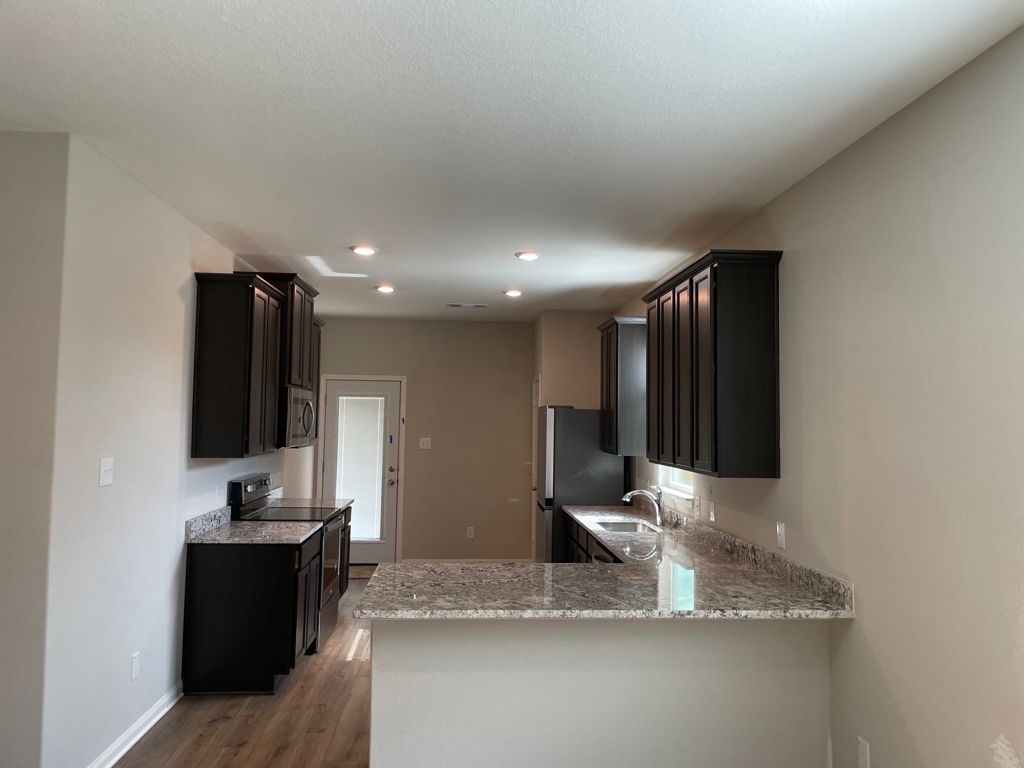 109 Declaration Lane Liberty Hill, TX 78642 - Photo 9 of 24 Kitchen with light stone countertops, stainless steel appliances, a peninsula, dark wood-type flooring, and dark cabinets