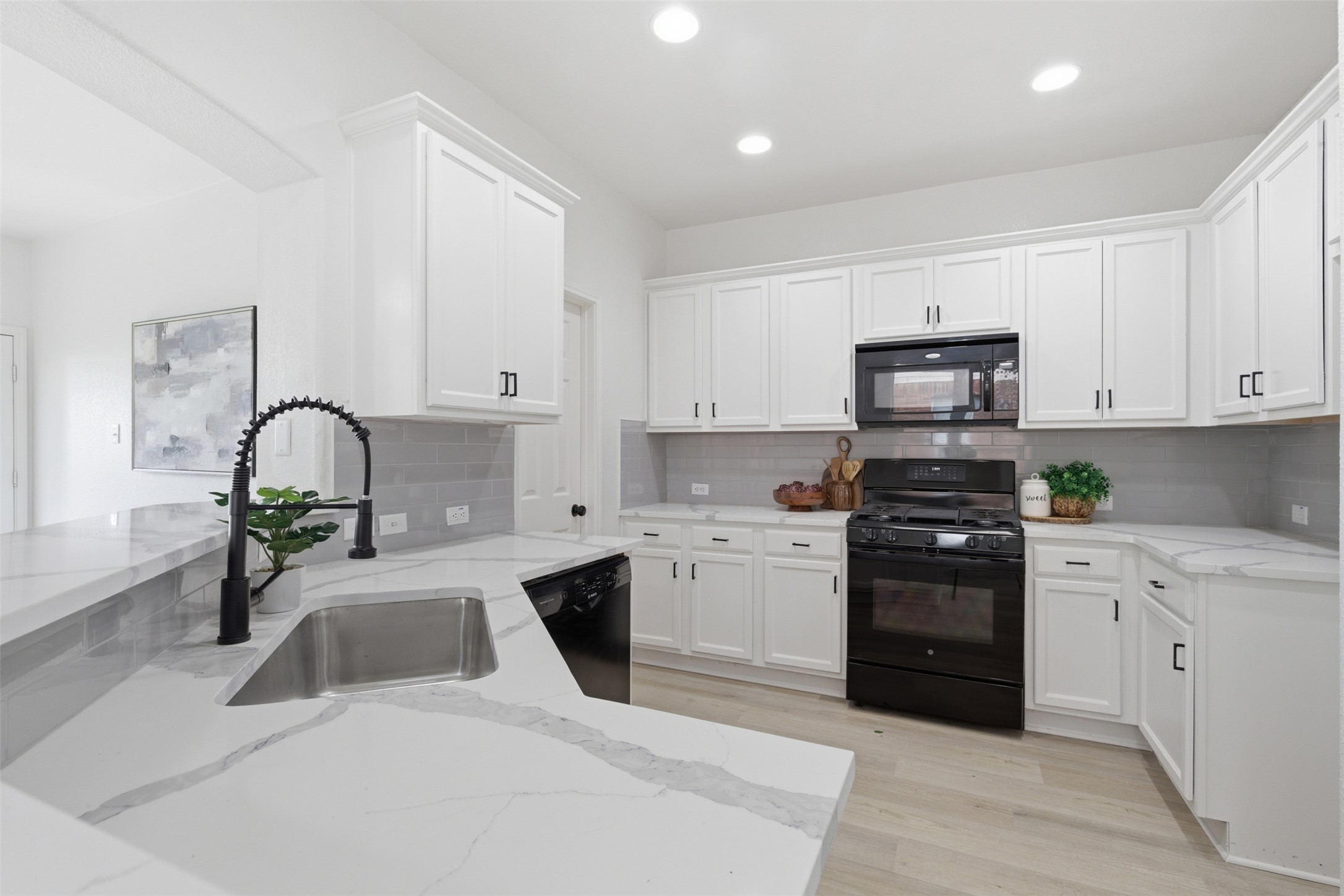 461 Hot Spring Valley Buda, TX 78610 - Photo 6 of 25 The kitchen features white cabinetry, a stainless steel sink with a black gooseneck faucet, light-colored flooring, and a black range with a matching microwave above it