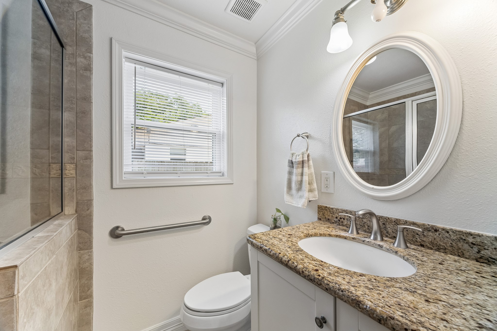 413 Mebane Lane Rosenberg, TX 77471 - Photo 21 of 30 This bathroom features a sleek design with a granite countertop, undermount sink, and oval mirror. It includes a glass-enclosed shower, a window for natural light, and modern fixtures, creating a bright and functional space.