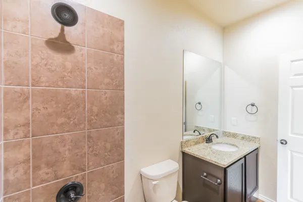 a bathroom with a granite countertop bathtub shower sink vanity mirror and toilet