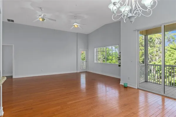 an empty room with wooden floor chandelier fan and windows