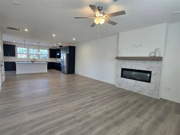 a view of an empty room and kitchen with wooden floor
