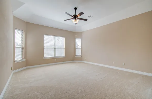an empty room with chandelier fan and windows
