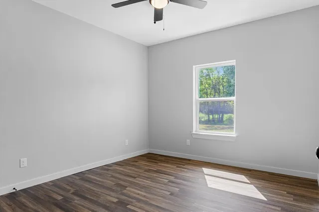 an empty room with wooden floor chandelier fan and windows
