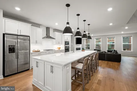 a kitchen with stainless steel appliances kitchen island granite countertop a stove a refrigerator a sink a dining table and chairs with wooden floor