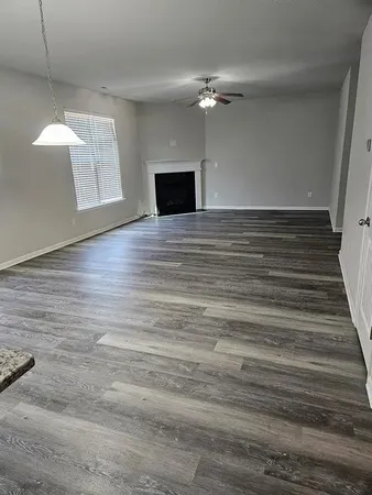 a view of an empty room with wooden floor and fan