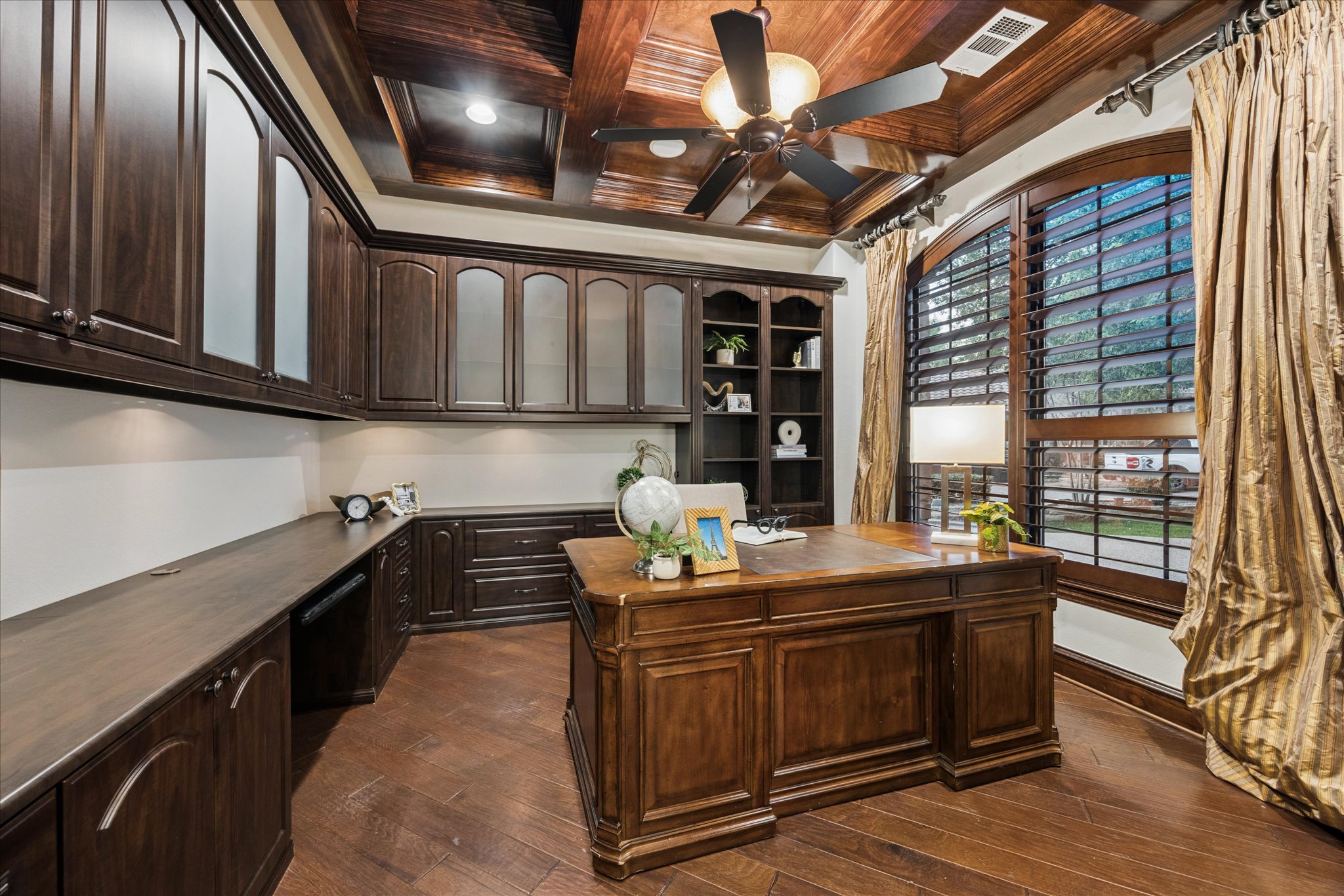 11805 Ranchview Court Austin, TX 78732 - Photo 16 of 36 Dedicated office space featuring extensive built-in dark wood cabinetry with glass-front uppers, a built-in bookshelf, a coffered wood-paneled ceiling, and wood-finish flooring