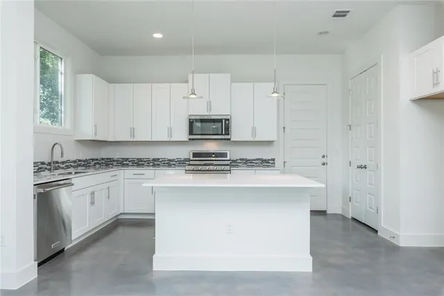 a kitchen with stainless steel appliances granite countertop a stove top oven a sink and white cabinets