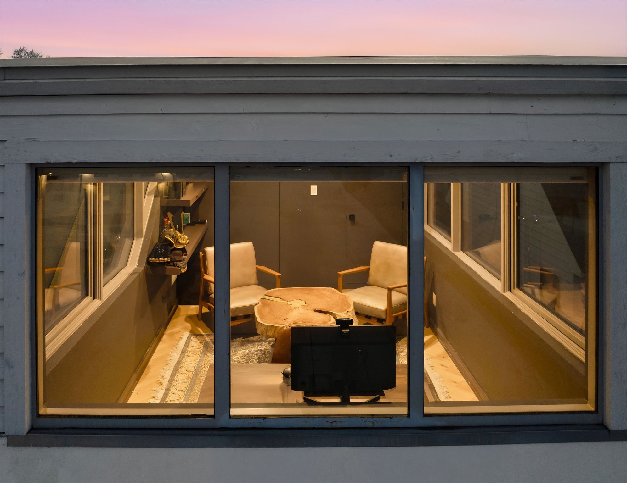 2615 Yupon Street Houston, TX 77006 - Photo 14 of 50 Elevated for ultimate privacy, this second-floor study features a wall of gridded windows that frame a serene evening sky. The sophisticated interior includes a live-edge wood table and modern lounge seating, creating a refined atmosphere for quiet focus or intimate conversation. Built-in shelving and designer finishes highlight the meticulous craftsmanship found throughout this 2022 custom estate.