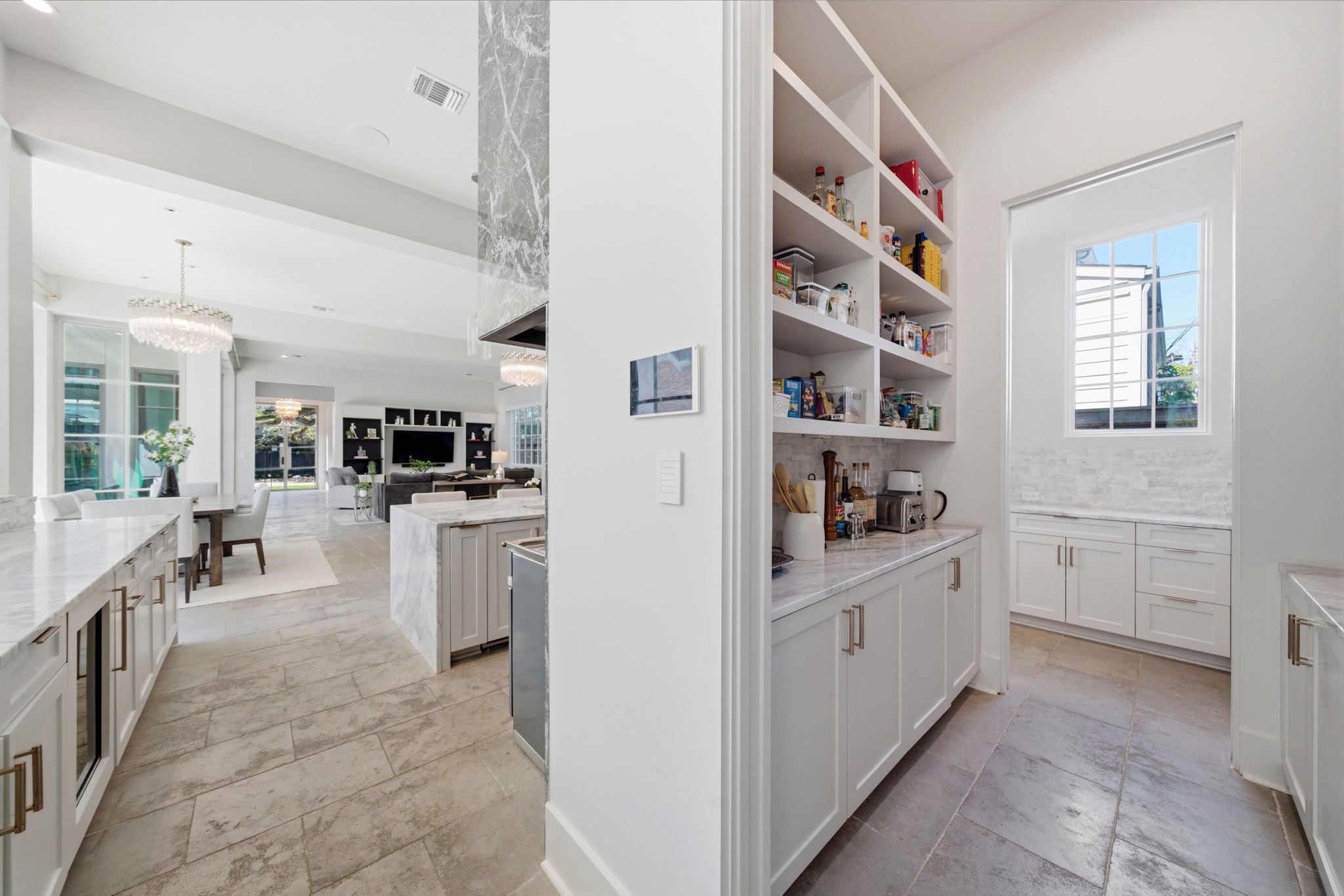 2615 Yupon Street Houston, TX 77006 - Photo 19 of 50 Spacious walk-in pantry offers exceptional organization with floor-to-ceiling open shelving and a dedicated appliance center. White custom cabinetry and marble countertops flow through the workspace, while a large window provides natural light and views of the picturesque street. This functional area connects the gourmet kitchen to a secondary prep space, ensuring every culinary need is met with ease and style.