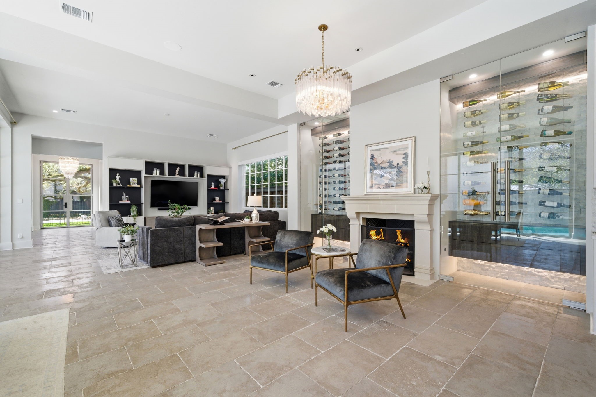 2615 Yupon Street Houston, TX 77006 - Photo 25 of 50 Glass-enclosed wine room serves as a breathtaking architectural centerpiece, featuring wall-mounted displays and ambient lighting for a premier collection. This climate-controlled space anchors the formal lounge, where a stone-clad fireplace and velvet seating offer a sophisticated retreat. Large-format stone floors and a cascading crystal chandelier enhance the luxurious, open-concept layout.