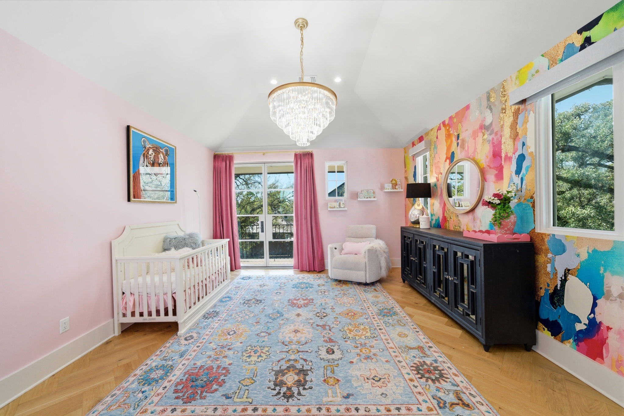 2615 Yupon Street Houston, TX 77006 - Photo 27 of 50 Vaulted ceilings and a cascading crystal chandelier elevate this designer secondary bedroom, while a vibrant abstract accent wall adds a bold, contemporary flair. Herringbone white oak floors flow toward a private balcony through steel and glass doors, offering serene views of the picturesque street. This light-filled retreat includes a spacious walk-in closet and a refined ensuite bath for ultimate comfort.