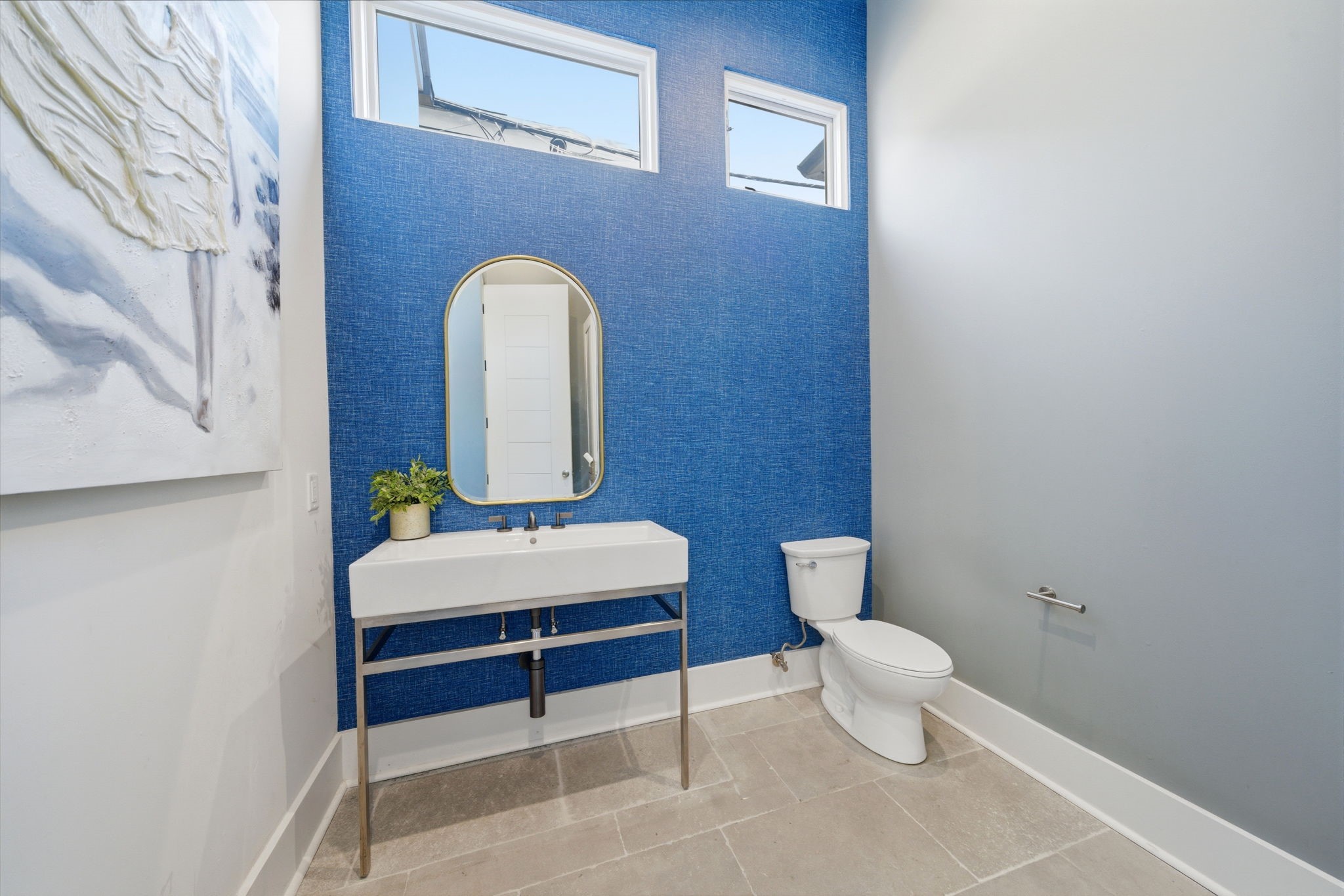 2615 Yupon Street Houston, TX 77006 - Photo 33 of 50 Designer half bath makes a bold statement with textured cobalt blue wallpaper and a modern trough-style floating sink. Elevated by high ceilings and dual transom windows, the space features a gold-framed arch mirror and sleek wall-mounted fixtures. Large-format stone tile flooring and a minimalist layout ensure this guest retreat is both sophisticated and functional.