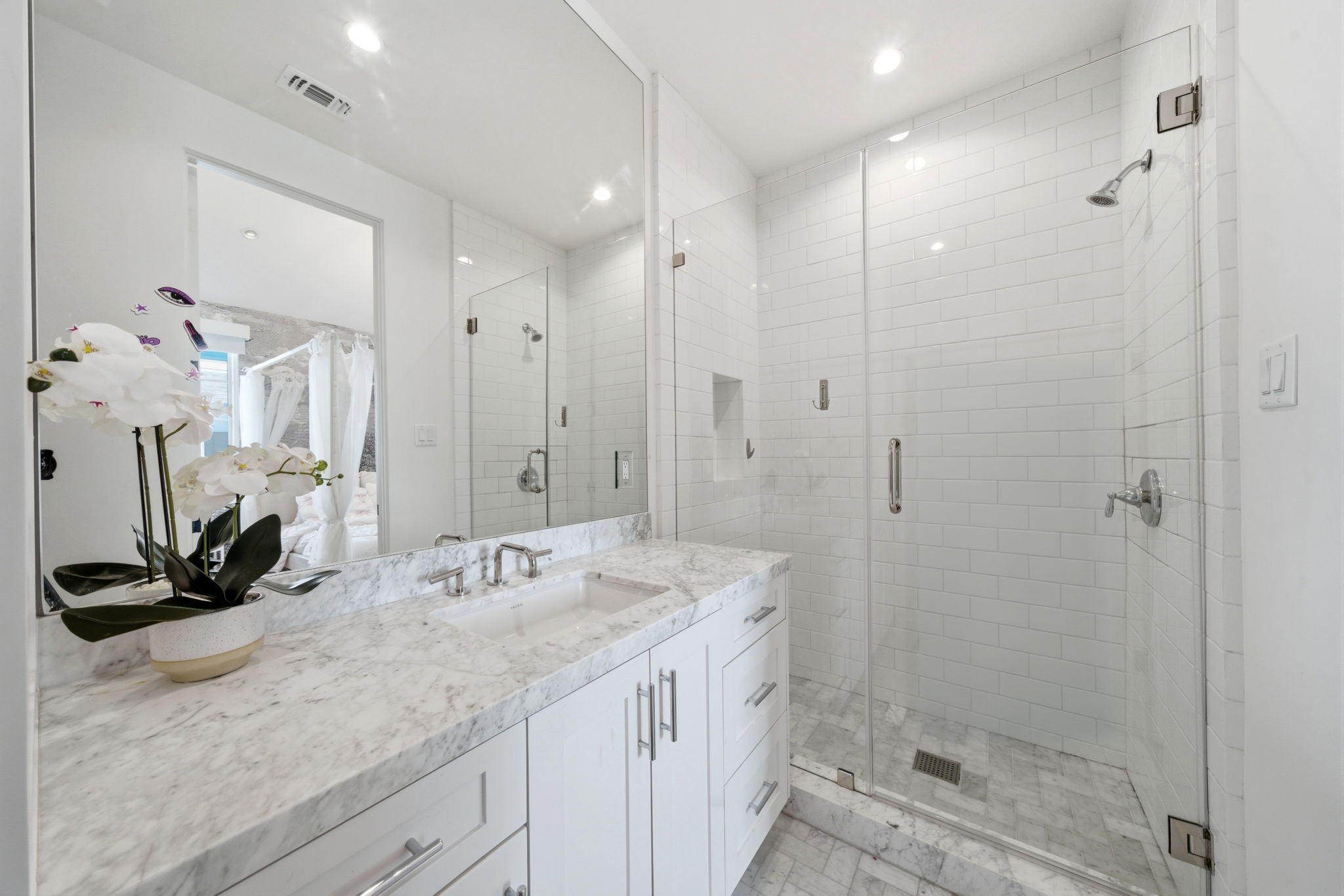 2615 Yupon Street Houston, TX 77006 - Photo 35 of 50 Crisp white custom vanity with a thick marble countertop and an under-mount sink anchors this spa-inspired ensuite bathroom. A glass-enclosed shower features timeless subway tile walls and a grey marble mosaic floor, providing a sophisticated retreat. Large-format stone tile flooring and a frameless mirror enhance the bright, airy feel of this contemporary space.