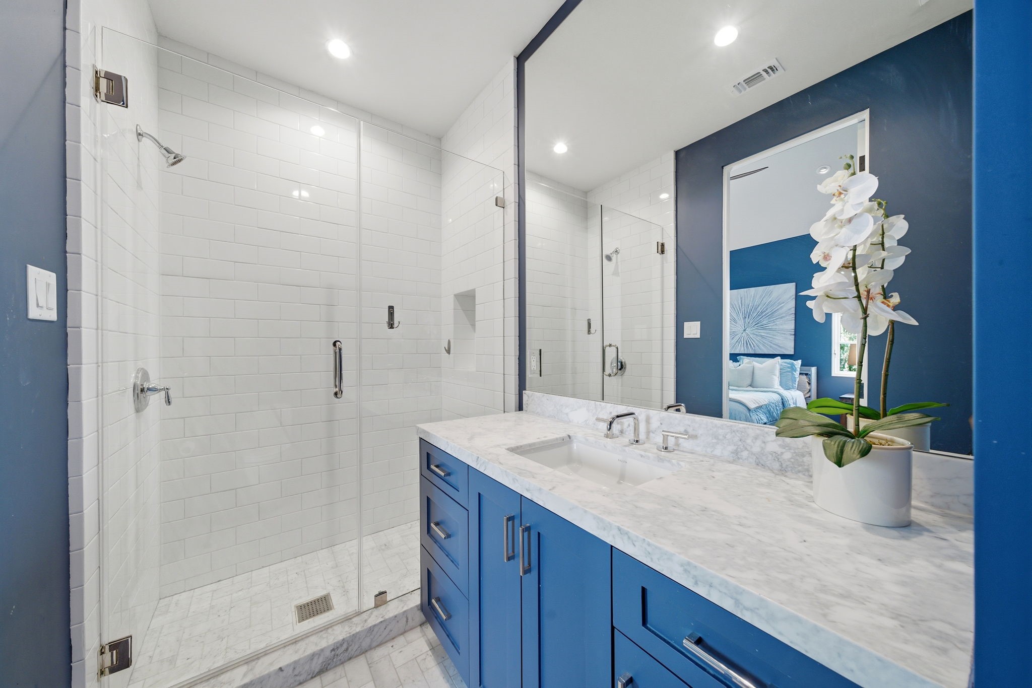 2615 Yupon Street Houston, TX 77006 - Photo 36 of 50 Vibrant cobalt blue walls and crisp white subway tile create a bold contemporary contrast in this sophisticated ensuite bath. The custom navy vanity is topped with a thick marble counter and a modern trough-style sink, while the glass-enclosed shower features a herringbone marble floor and polished chrome fixtures. Large-format stone tile and an expansive frameless mirror enhance the bright, airy feel of this luxury 2022 custom estate retreat.