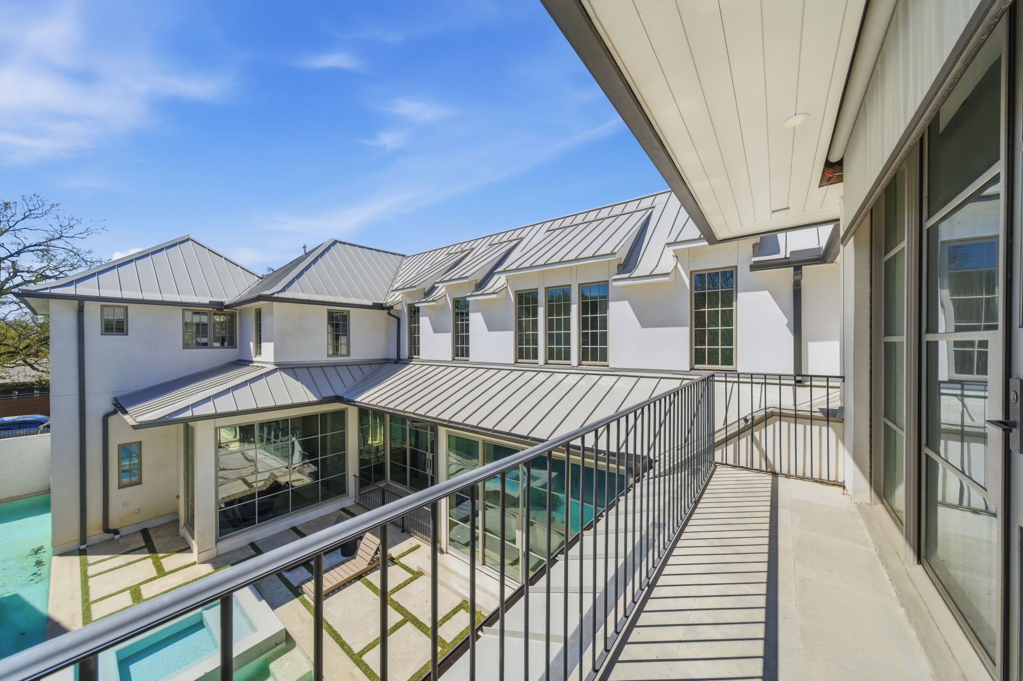 2615 Yupon Street Houston, TX 77006 - Photo 43 of 50 Aerial view from the private balcony reveals the striking contemporary architecture of this 2022 custom estate, centered around a geometric heated pool and spa. The expansive courtyard design features a sleek metal roof and floor-to-ceiling glass walls that connect the home gym and living areas to the outdoor oasis. Modern stone pavers with turf accents lead to a sun-drenched lounging deck, emphasizing the luxury indoor-outdoor lifestyle in this premier Montrose location.