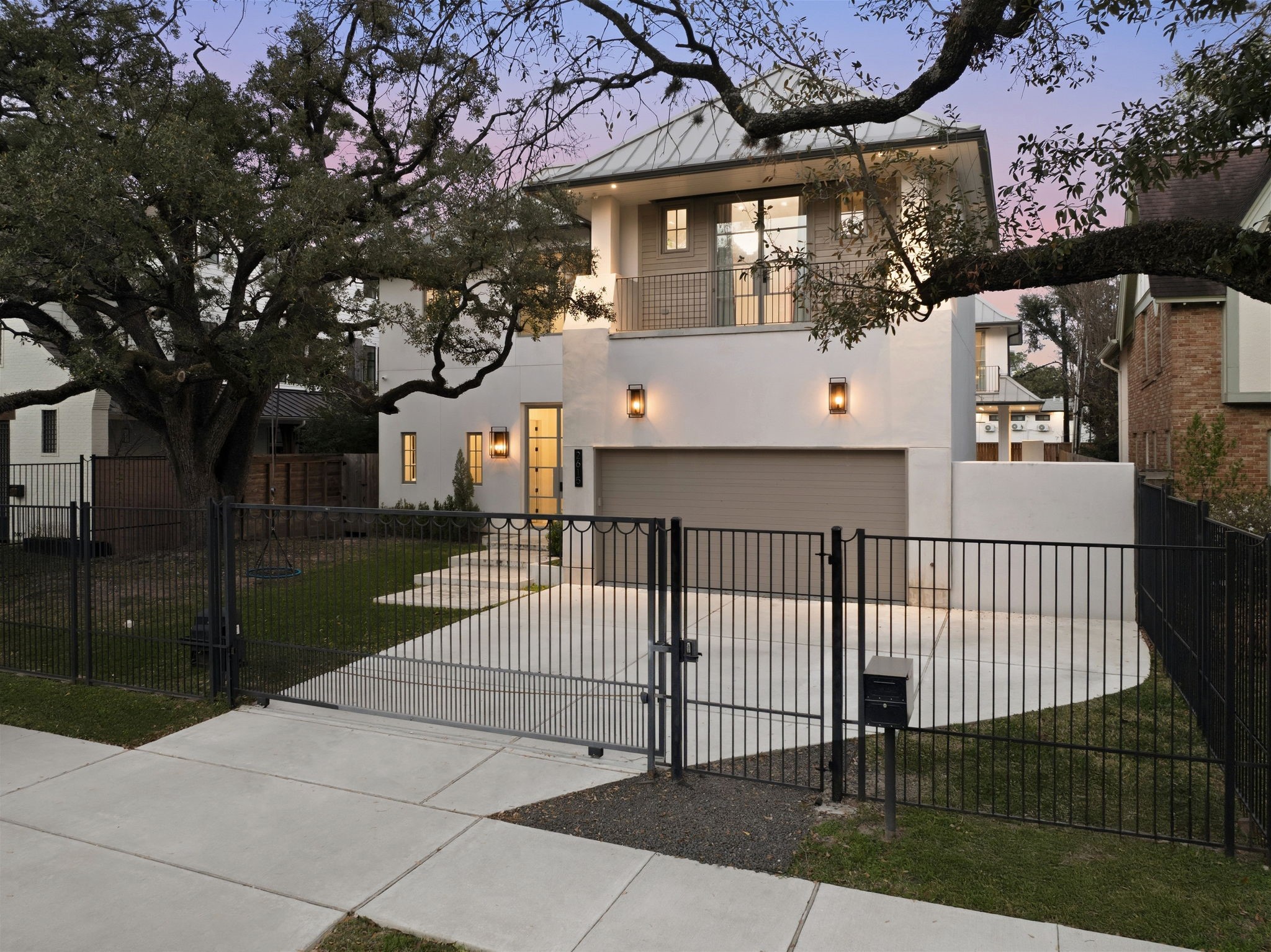 2615 Yupon Street Houston, TX 77006 - Photo 7 of 50 Securely positioned at 2615 Yupon St, this 2022 custom estate features a striking contemporary facade protected by a modern black iron security gate and private driveway. Stately oak trees frame the sleek stucco exterior, highlighting the second-story balcony and designer lantern lighting. The built-in 3-car garage and floating concrete walkway emphasize the home's high curb appeal.