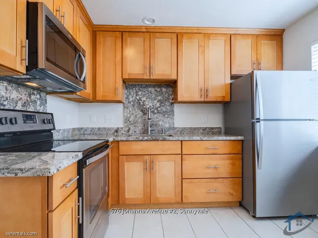 a kitchen with stainless steel appliances granite countertop a refrigerator a sink dishwasher and wooden cabinets with a large window